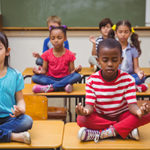 Pupils meditating in lotus position on desk in classroom at the elementary school