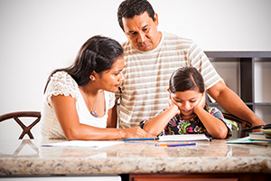 A photograph of parents helping their daughter who is struggling with her homework.