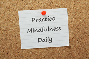 The phrase Practice Mindfulness Daily on a piece of paper pinned to a cork notice board. A mental state achieved by focusing awareness on the present through meditation
