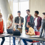 Casual students with female teacher in modern college building, woman in her 50s explaining to young people in their 20s