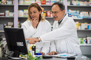 Senior pharmacist showing to his young colleague how to work on computer