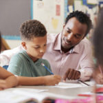 Male teacher working with elementary school boy at his desk