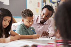 Male teacher working with elementary school boy at his desk