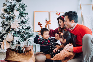 Christmas lifestyle theme. Happy Asian family decorating Christmas tree together in the living room at home. They are putting on various baubles and ornaments and enjoying their holiday