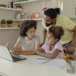 Two African American Parents Helping Their Daughter With Homework while using Laptop in the Kitchen at Home