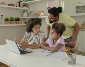 Two African American Parents Helping Their Daughter With Homework while using Laptop in the Kitchen at Home