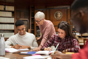 Two multiethnic students in reading hall with senior professor studying at a table with books. College and ADHD.