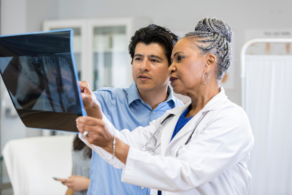 Pediatrician shows concerned father foot x-rays A concerned mid adult father points to a set of x-rays as a pediatrician shows him the images and shares the discovery. They are standing in an exam room. His teen daughter sits on a bed in the background.
