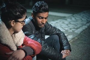 Asian, Indian unhappy young man and woman discusses something serious together and they sit in park at night.