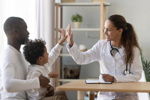 Happy mixed race african cute little child boy give high five to female doctor pediatrician welcome small kid patient and his dad at medical check up appointment, children medical health care concept