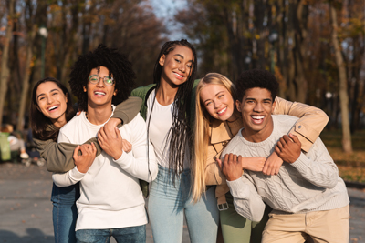Positive group of multiracial young friends having fun at public park, hugging and smiling