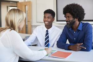 Father And Teenage Son Having Discussion With Female Teacher At High School Parents Evening