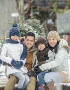 An Asian family is outdoors at a tree farm .They are posing for a picture while it snows.