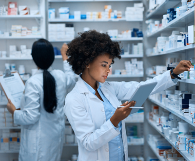 Shot of a young woman doing inventory in a pharmacy on a digital tablet with her colleague in the background