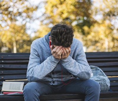 Teenager sits on a bench in the park and listen to music and learning for exame