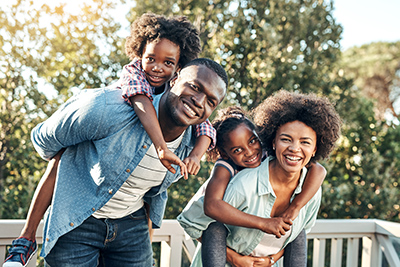 Portrait of a cheerful young mother and father giving their children piggyback rides outside during the day