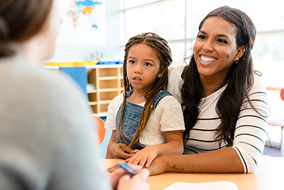 The mid adult single mother holds her anxious preschool age daughter in her lap at the parent teacher conference.