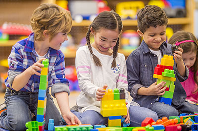 A multi-ethnic group of elementary age children are playing with plastic blocks in class.