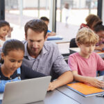Teacher helping young students using laptops in class